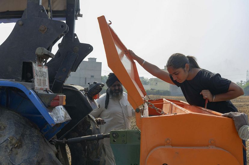 Amandeep lifts a lid from an orange seeder machine and peers inside of the machinery. Her father is nearby.