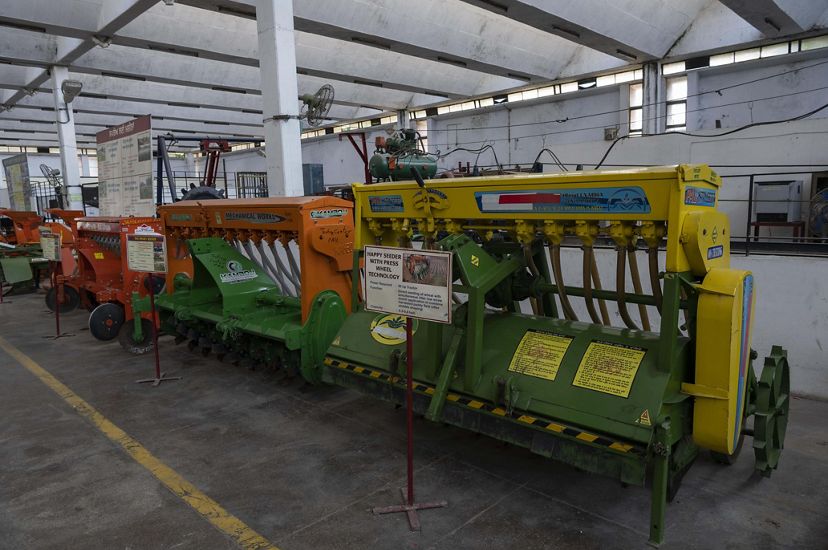 In a long university building, three large seeder machines of different colors sit next to each other, full of rotors and hoses.