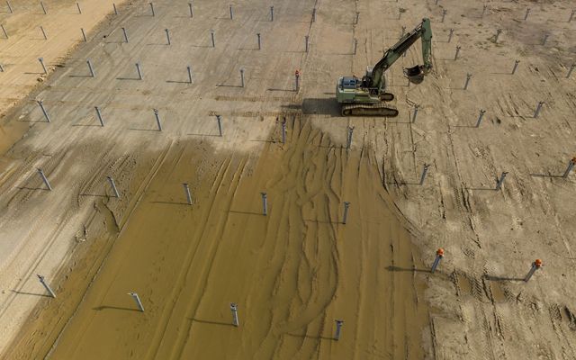 Aerial view of a large construction digger in the midst of a soon-to-be solar field.