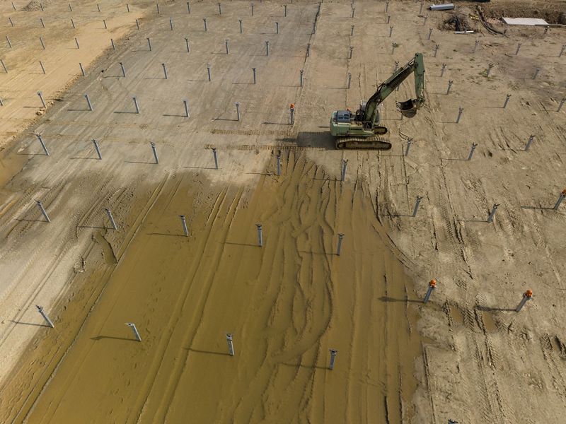 Aerial view of a large construction digger in the midst of a soon-to-be solar field.