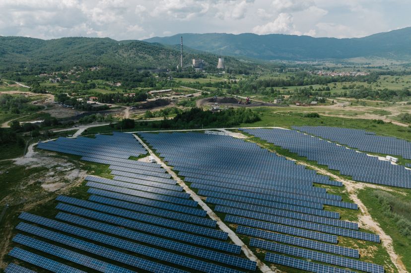 Lines of solar panels fill a grassy field with mining infrastructure in the background.