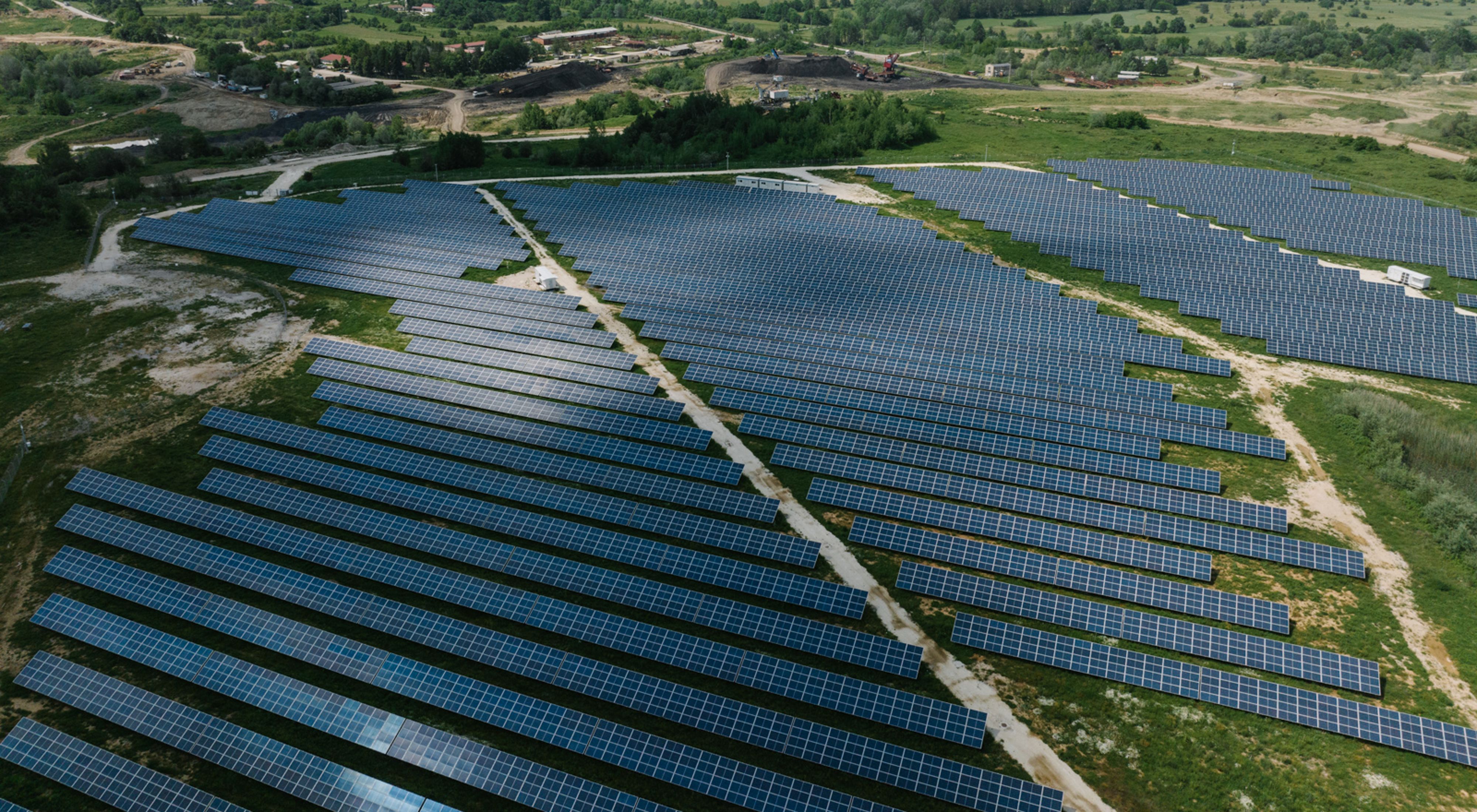 A vast expanse of solar panels in the foreground leads to the base of a now-defunct coal plant in North Macedonia.