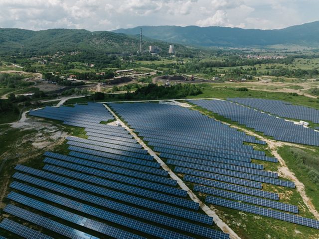 Lines of solar panels fill a grassy field with mining infrastructure in the background.