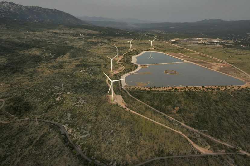 Aerial view of wind turbines at the edge of a manmade body of water at a power plant.