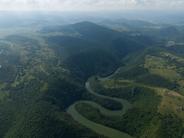Aerial of a river full of oxbow curves brushing up against hilly terrain and farmland.