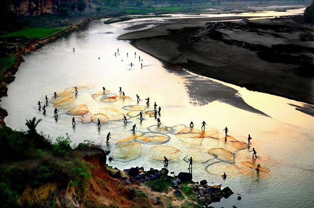 Aerial view of people standing in a West Bengal river in India, casting nets for fishing.