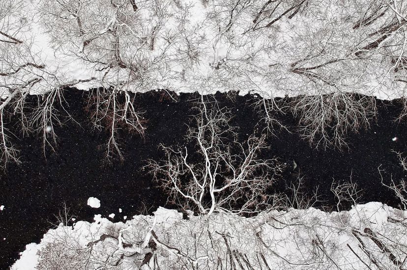 Looking down on a wide creek. The dark water splits the middle of the image, running between snow covered banks.
