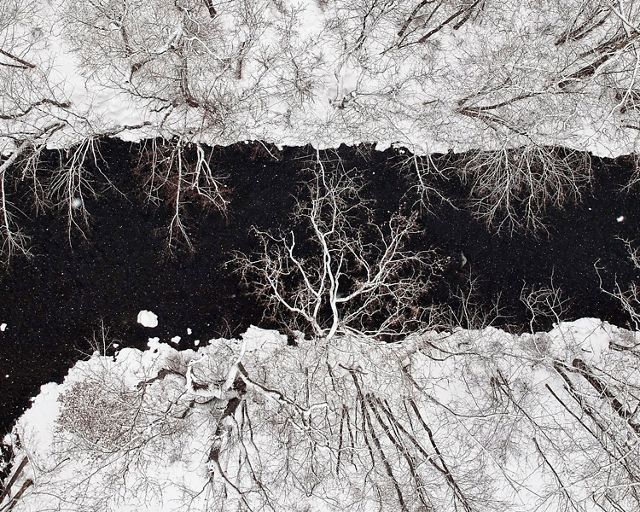 Looking down on a wide creek. The dark water splits the middle of the image, running between snow covered banks.