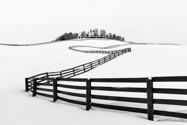 A fence winds and bends up a snow covered hill towards the house sitting atop it.