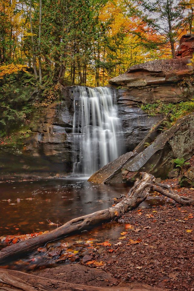 A waterfall in Michigan's Upper Peninsula in autumn. The surrounding trees are covered in colorful leaves. 