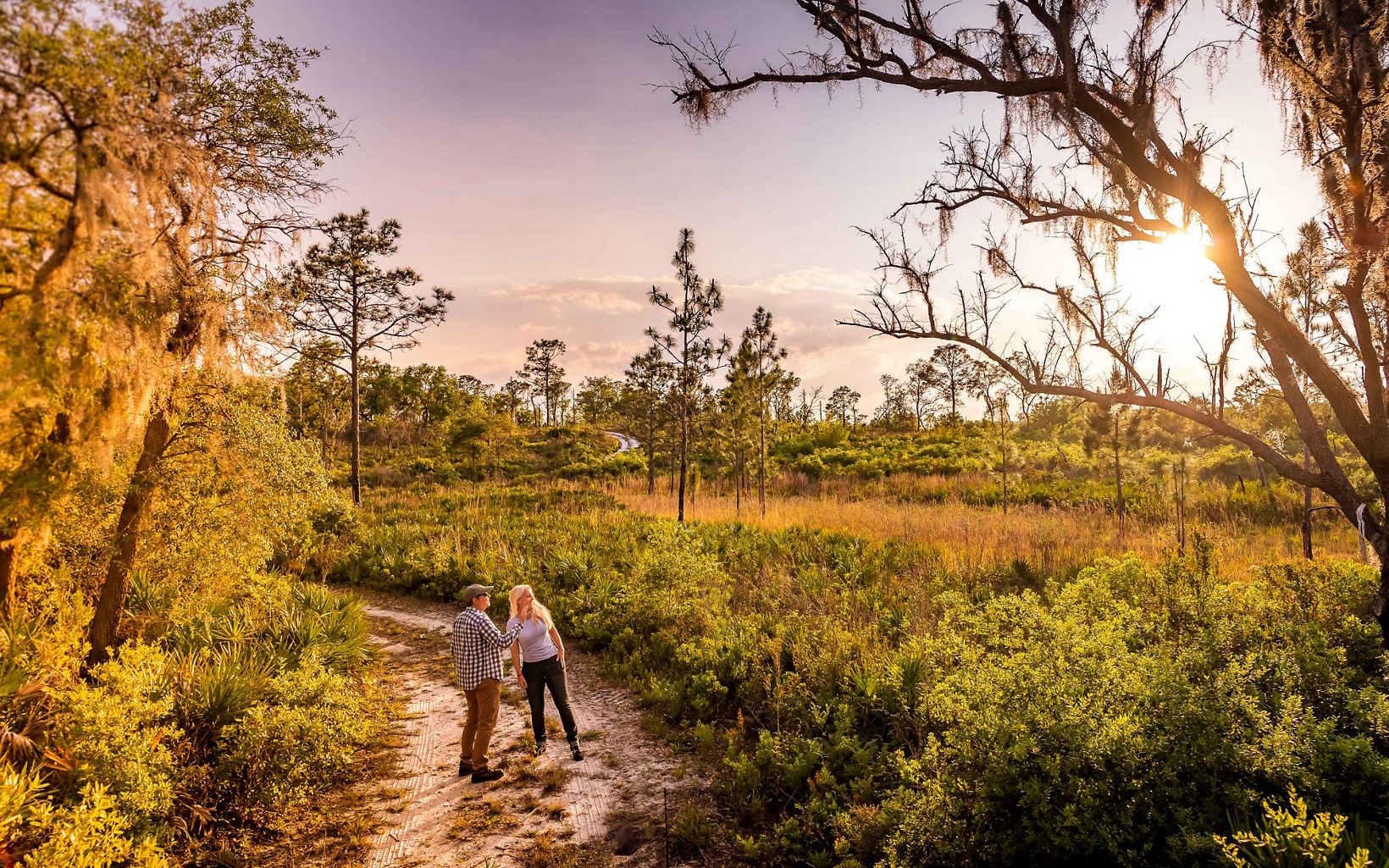 Two hikers enjoy a trail through trees and shrubs at Tiger Creek Preserve during sunset.