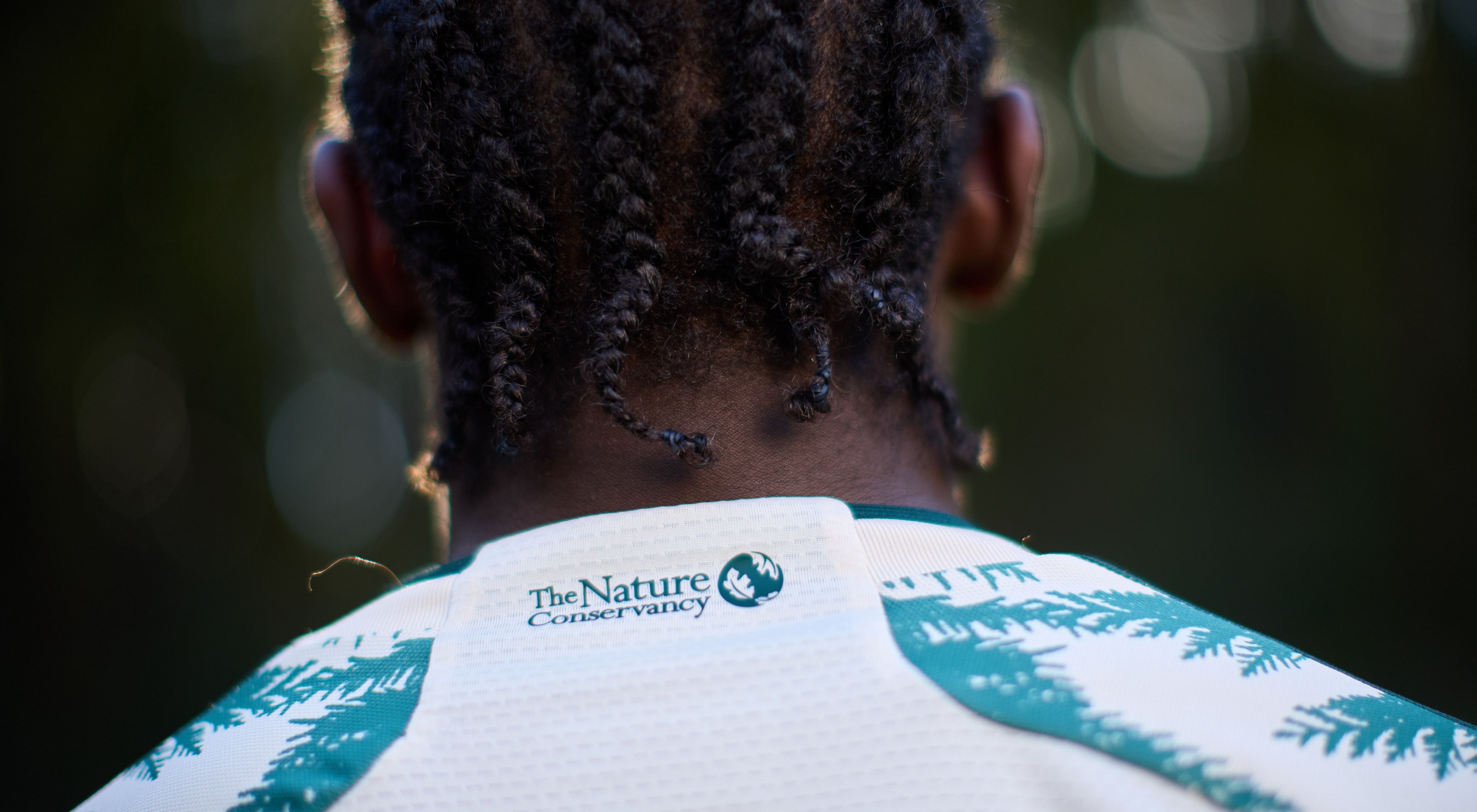 A person with their back facing the camera showing the TNC logo on the back of their shirt collar. 