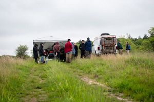 A group of people stand near a makeshift lab set up outdoors in an open prairie.