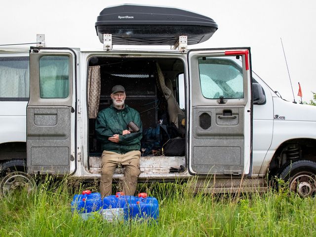 A man sits inside the open side doors of an Econoline van.