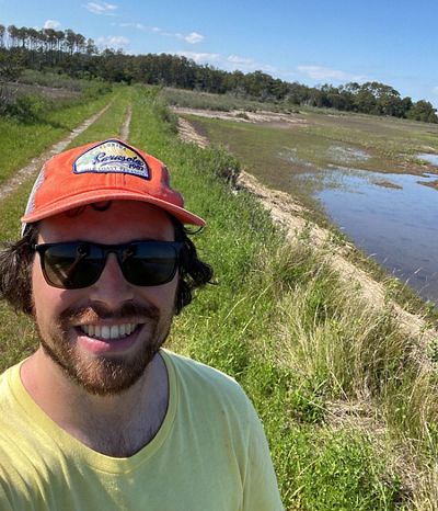 Candid selfie headshot of Ben Nettleton taken outdoors standing next to a wetland.