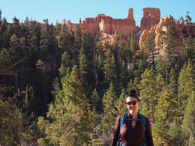 Candid headshot of Danielle Kulas standing outside against a backdrop of tall fir trees in Bryce Canyon.