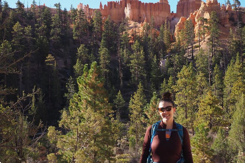 Candid headshot of Danielle Kulas standing outside against a backdrop of tall fir trees in Bryce Canyon.
