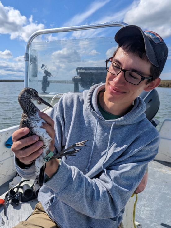 Candid portrait of Mario Balitbit sitting in a boat holding a young shorebird.