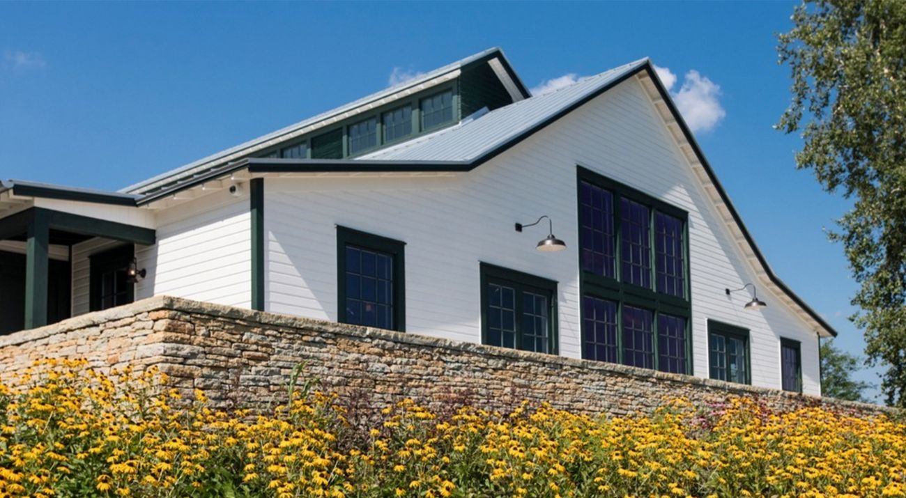 An image of a grand farmhouse with flowers blooming in front of it.