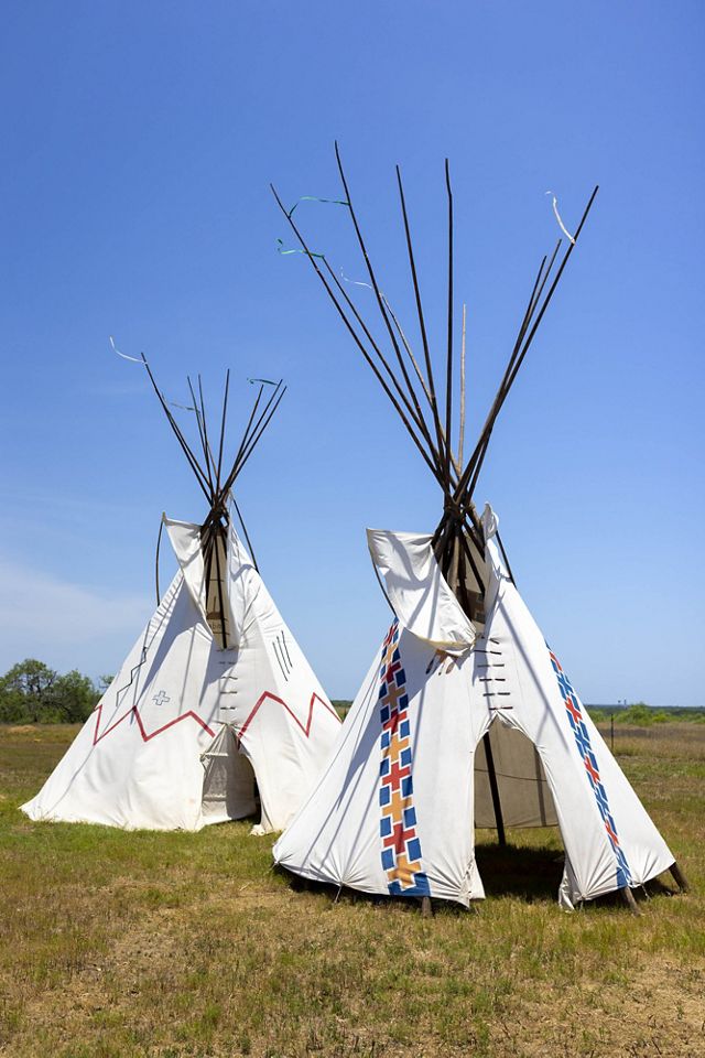 2 fully erected tepees stand with white clothes, decorated with geometric patterns