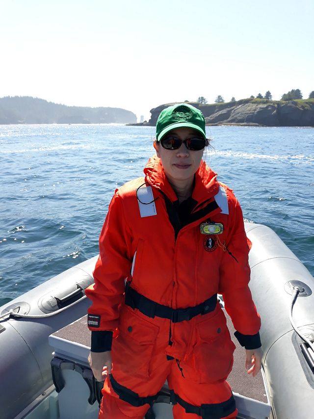 Jennifer Lee Clinchy wears an orange jumpsuit and stands in a small boat on a body of water.