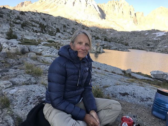 Martha Kongsgaard sits in a rocky area with a small lake and a mountain range in the background.