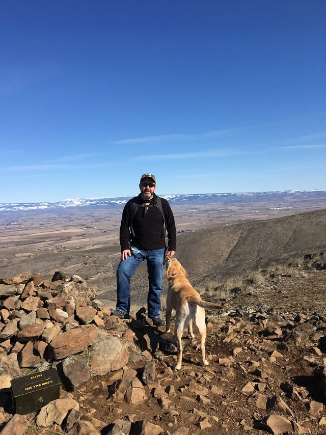 Paul Jewell stands with his dog atop a mountain.