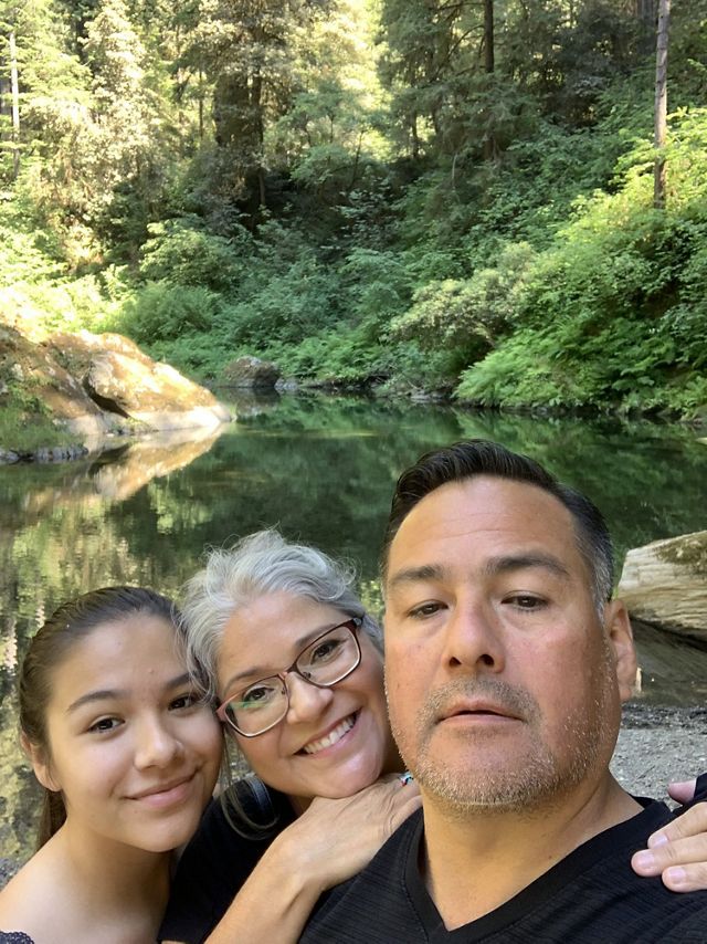 A family takes a selfie in front of a stream.