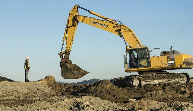 A yellow excavator digs through piles of dirt and mud.