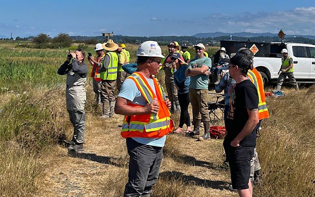 Many people stand outside in a marsh area.