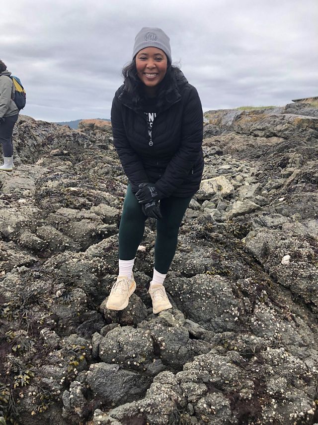 Leah Palmer stands on a rocky shore and smiles for the camera.