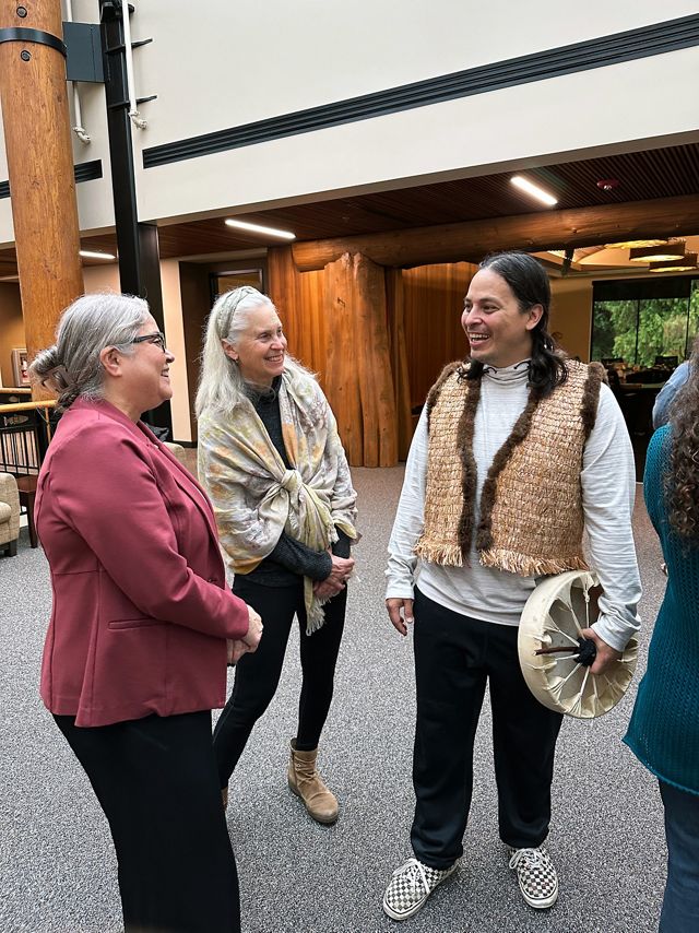 Three people stand together talking and smiling during a celebratory gathering.