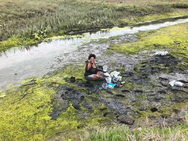Dr. Tiara Moore sits in a muddy field and collects samples.
