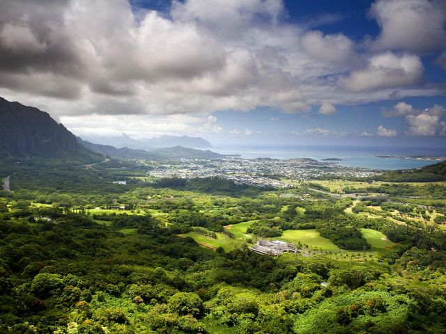 Landscape view overlooking a wide green valley on Oahu, Hawaii, with housing and the ocean in the distance.