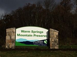 A large sign welcoming visitors to Warm Springs Mountain Preserve. Two stone pillars support a sign reading, Warm Springs Mountain Preserve. The TNC globe logo is at the lower right.