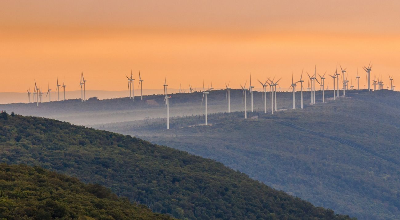 A line of wind turbines marches along a misty blue ridge in the Appalachian Mountains of West Virgina.