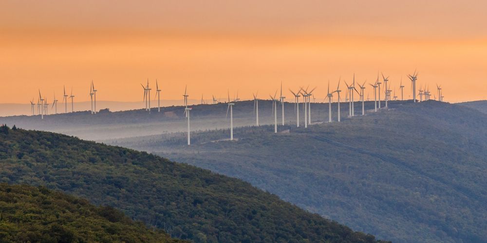View of a vast ridgetop with rows of wind turbines on it.
