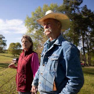 A mand and a woman stand together by a barbed wire fence.