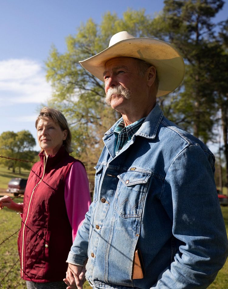 A mand and woman stand together by a fence.