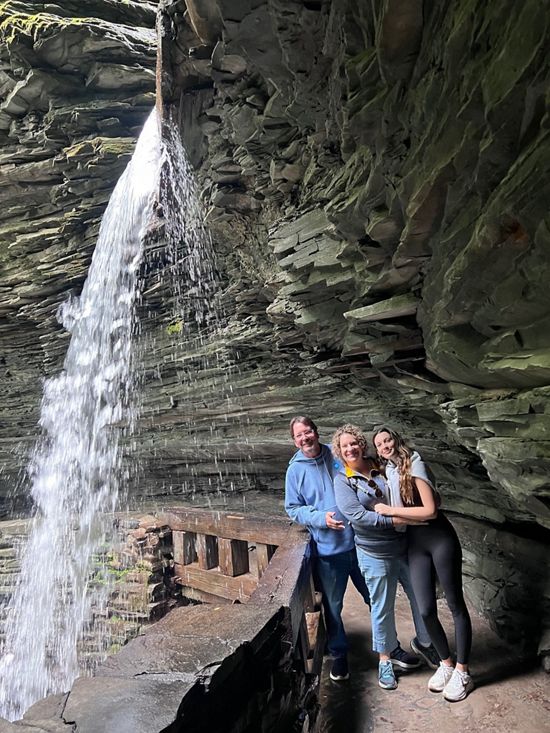 Three people stand on a path under a waterfall.