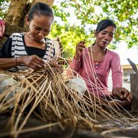 Two women sit on the ground and weave rattan baskets in Borneo.
