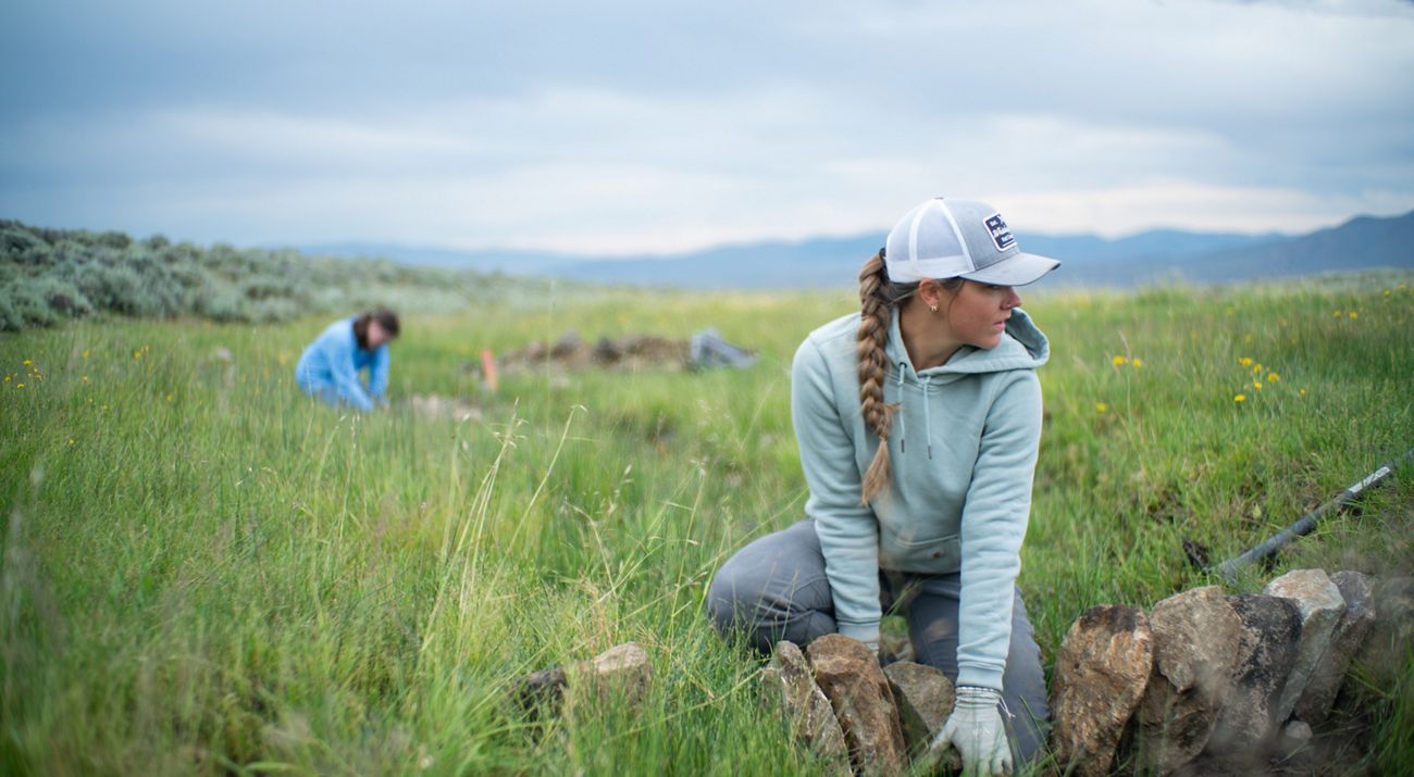 Two Youth Employment Program crew members place rocks in a grassy field to create a wet meadow.