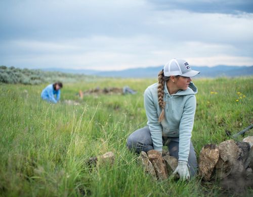 Two Youth Employment Program crew members place rocks in a grassy field to create a wet meadow.