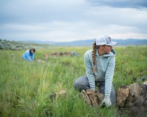 Two Youth Employment Program crew members place rocks in a grassy field to create a wet meadow.