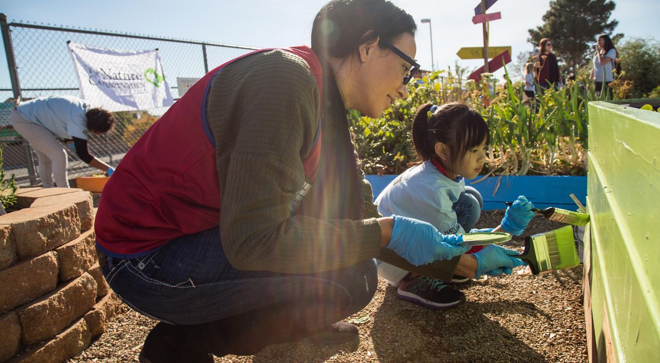 An adult and a child paint a garden box green.