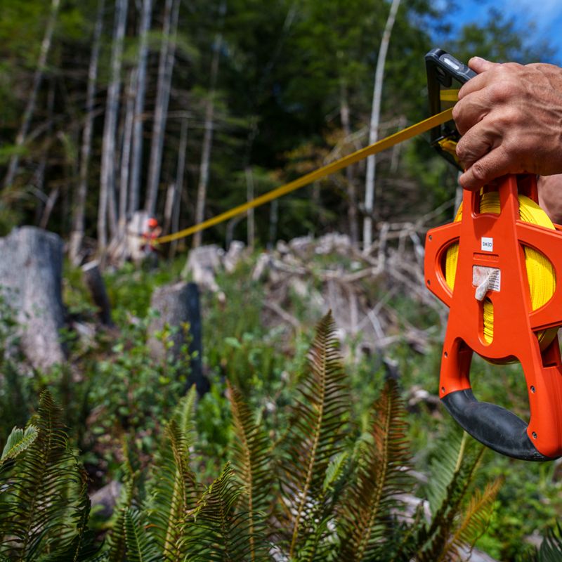 A close up of a person's hands using a tape measure for forest management in Canada.