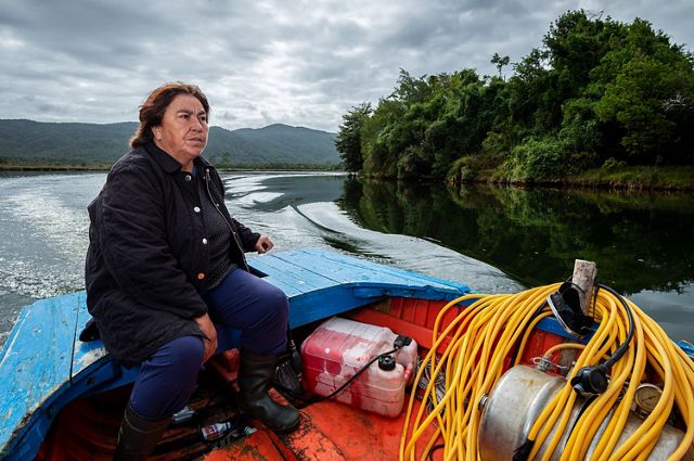 portrait of Adelaida Arriaza sitting on a blue wooden boat in a river.