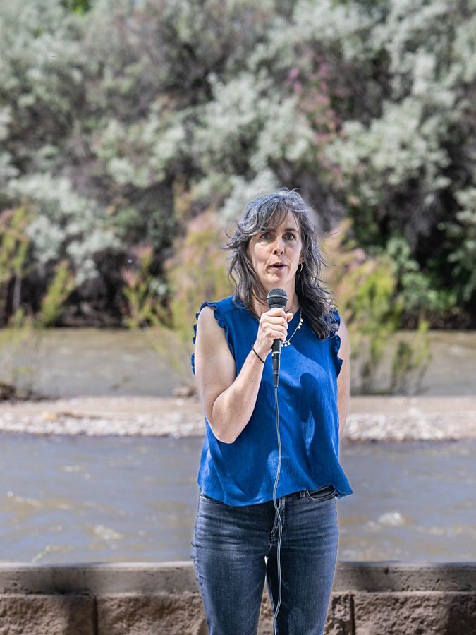 A woman speaking into a microphone in front of a river.