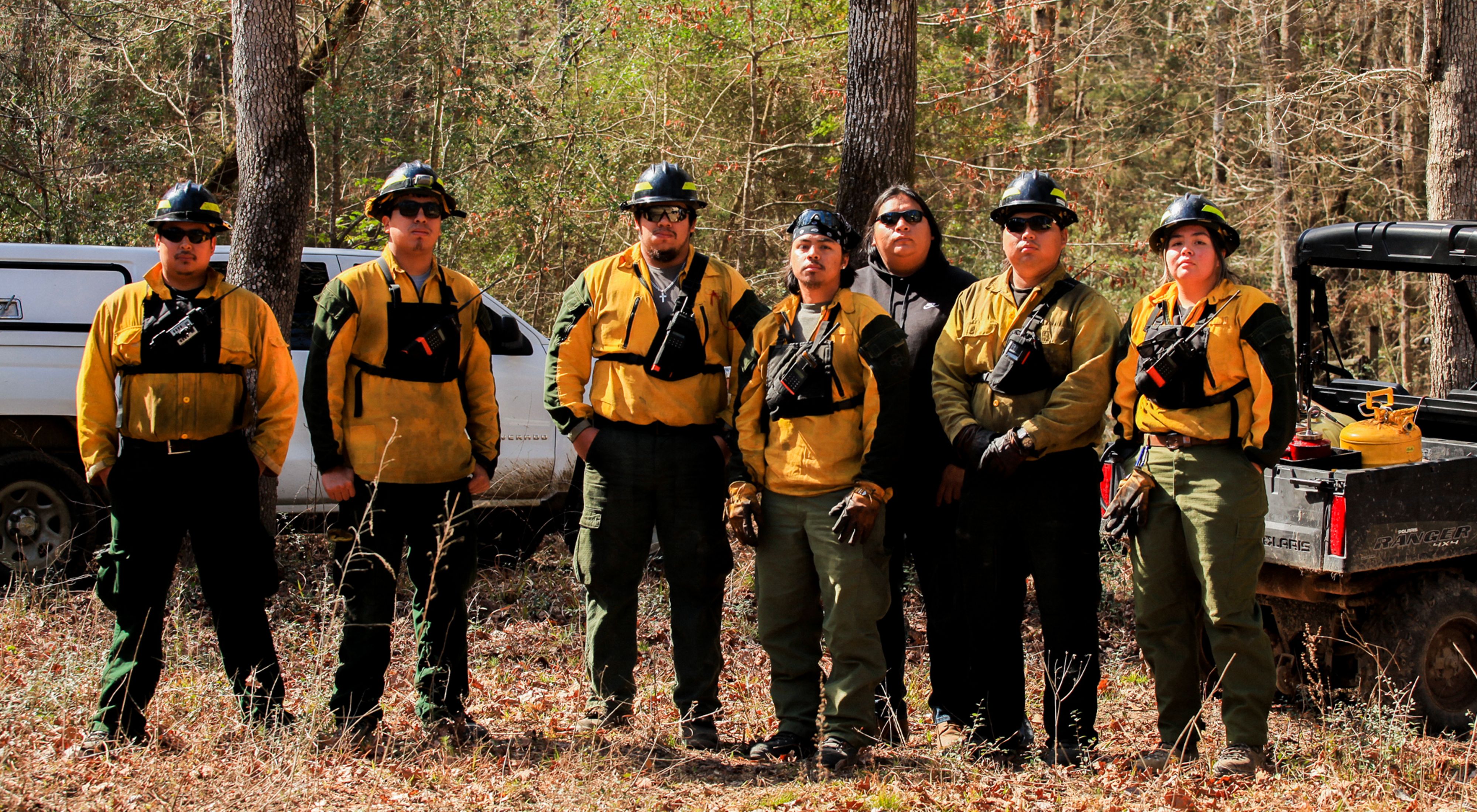 Seven members of the Alabama-Coushatta Tribe of Texas Wildland Fire Management crew stand ready in their protective gear before a prescribed burn.