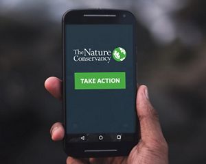 A hand holds a smartphone that has the TNC logo and the words 'Take Action' on the screen.
